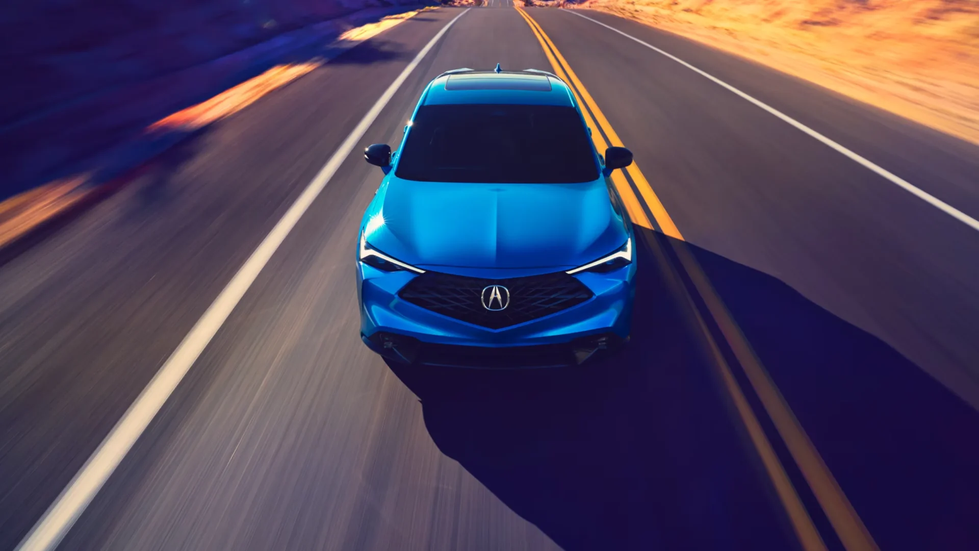 Acura ADX 2026 bleu vu de haut en circulation sur une route à double ligne jaune.