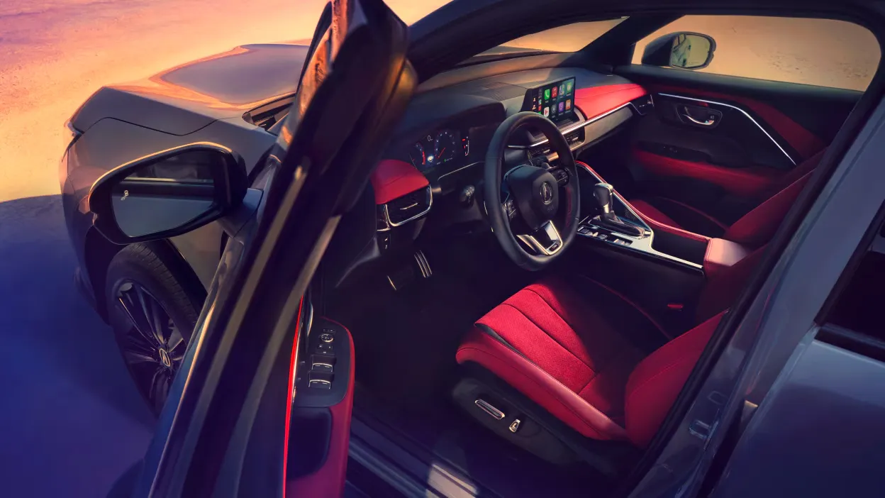 Habitacle de l’Acura ADX 2026 avec sièges rouges, volant et écran central, vu par la portière conducteur ouverte.